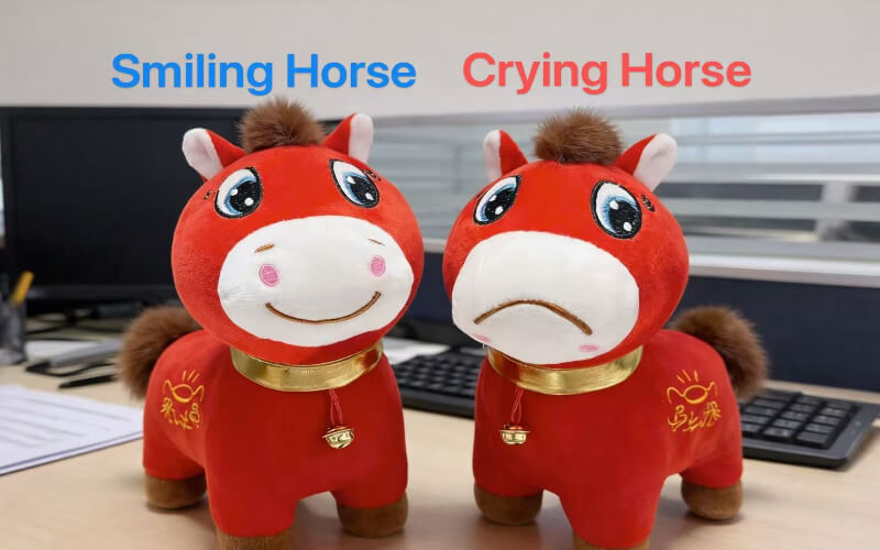 Cry cry horse plush toy displayed next to a smiling horse plushie, placed on an office desk for expression comparison.