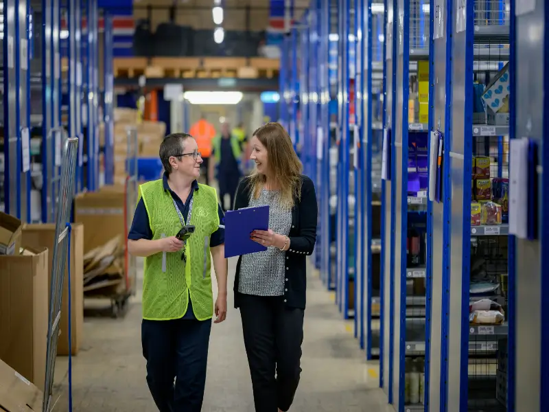 A warehouse worker scans a cardboard box with a barcode reader, showcasing the fulfillment process for a retailer
