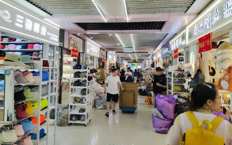 Inside Yiwu wholesale market showing hat and accessories booths with buyers and sellers